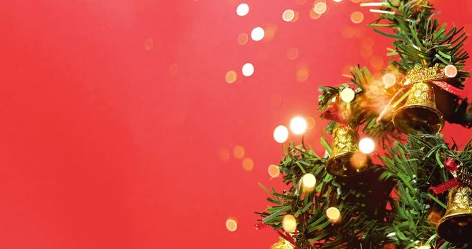 Christmas tree decorated with golden bells with bokeh lights on red background.