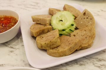 Popular Asian food, sliced Vietnamese pork sausage recipe (Cha lua) topping with sliced cucumber in white plate and spicy sauce. This menu is the most common type of sausage in Vietnamese cuisine.