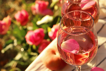 Glasses of delicious rose wine with petals outside, closeup. Space for text