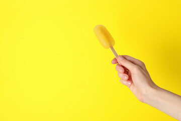Woman holding delicious ice pop on yellow background, closeup view with space for text. Fruit popsicle