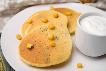 Tasty corn pancakes with sweet kernels and sauce served on table, closeup