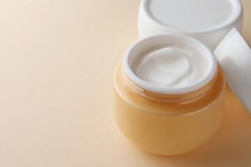 Jars of face cream on beige background, closeup. Space for text