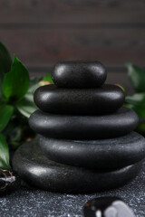 Stacked spa stones and bamboo leaves on black textured table, closeup