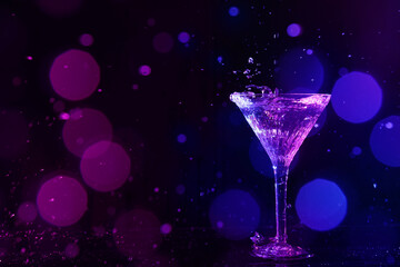 Glass of martini and splashes in neon lights on dark background, bokeh effect with space for text