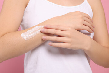 Fototapeta na wymiar Young woman applying body cream onto arm on pink background, closeup
