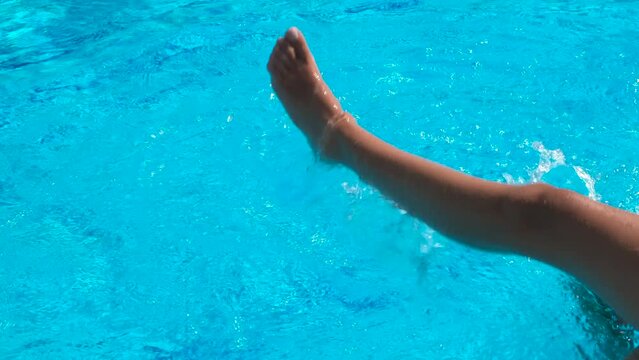 Kicking shaking foot in pool. A teen legs by the public pool kicking and shaking her feet under water in the sun rays.