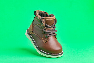 Leather baby boot with laces on a green background. Concept of modern fashion.