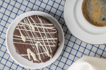 Top view of brown chocolate alfajor, typical candy in Argentina, with a cup of coffee on a checkered tablecloth.