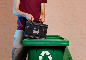 Man throwing old empty car battery in garbage disposal with recycling symbol  - obrazy, fototapety, plakaty