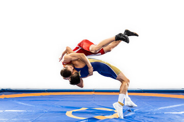 Two  strong men in blue and red wrestling tights are wrestlng and making a suplex wrestling on a yellow wrestling carpet