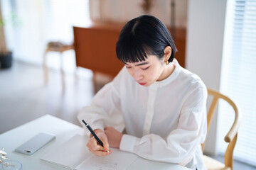 部屋でノートに書きものをする若い女性