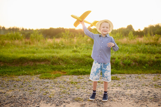 Happy boy playing with airplane model outdoors at sunset. The concept of relaxation, imagination, holidays, freedom.