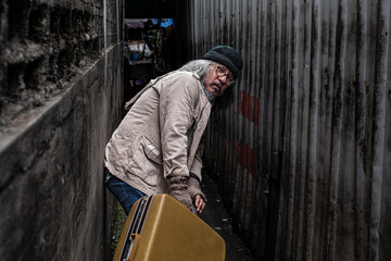 Asian homeless man dragging large suitcase in a narrow alley for to find rest, no home live on...