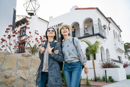 two smiling asian Japanese girl friends looking up at something interesting in the sky while taking relaxing stroll together at santa Barbara beach neighborhood in california usa