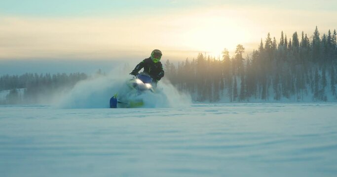 Rider on snowmobile leaving snowy powder trail driving on arctic circle woodland landscape at sunrise