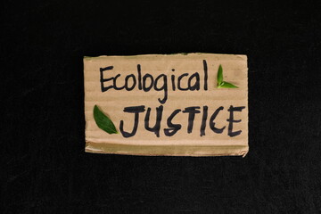 Ecological justice concept. Carton placard with handwritten message in dark black background.