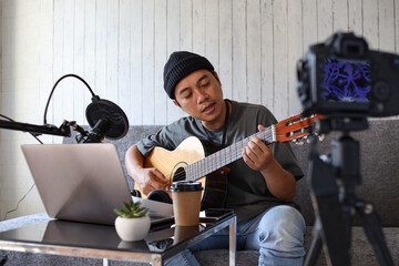 Asian influencer playing guitar during podcast or live video broadcast for the audience, recorded from digital camera at home