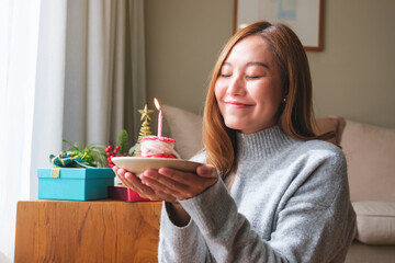 Fototapeta premium Portrait image of a young woman wishing and holding birthday cake with candle, Christmas holiday decoration at home