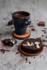 Cup of hot chocolate and pieces of chocolate brownie on light concrete background