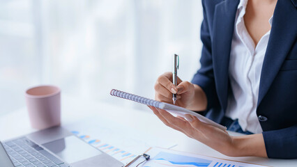 Close-up businesswoman sitting taking notes intensively and doing assigned tasks happily and purposefully.