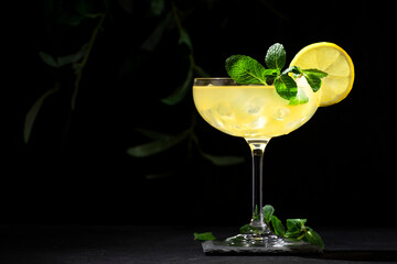White lady alcoholic cocktail with dry gin, liquor, lemon juice and ice in glass. Bartender pours cocktail from shaker into glass. Black background