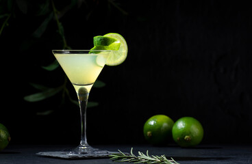 Gimlet alcoholic cocktail with dry gin, liqueur, lime juice and ice in glass garnished with lime zest. Black background