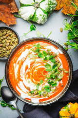 Pumpkin soup with seeds, cream and green pea sprouts. Winter or autumn healthy slow food. Soup bowl on gray table background. Top view