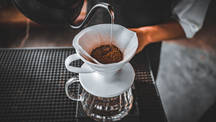 Hand Drip Coffee, Barista pouring hot water on roasted coffee ground with filter,and man is pouring hot coffee from the coffee pot into the white cup coffee on the table in the morning,vintage
