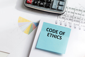 On a light desktop, a pen, paper clips and a white card with the text CODE OF ETHICS