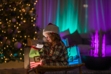 Fototapeta na wymiar Kid with present gift with magic light. Lighting present gift bag. Happy child in pajamas near Christmas tree at home with traditional Christmas tree.