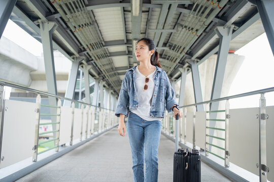 Young woman in casual clothes walking with luggage on walkway of the bridge in city, She is on her way to the airport.