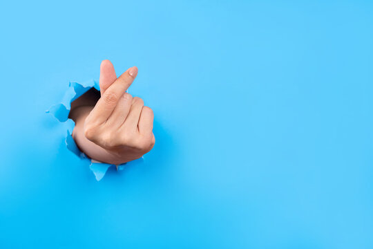 Human's hands showing symbol korean mini heart gesure through the torn holes of bright blue paper background. Creative art, copy space.