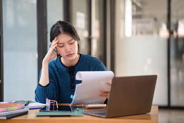Businesswoman looking stressed while holding paperwork or document at her desk. Woman looking...