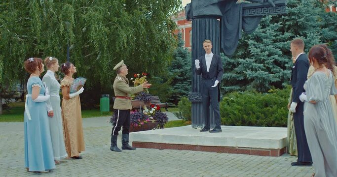 Meeting of nobles at a monument in a city park, a gentleman in a tailcoat speaks to ladies in beautiful dresses and a man in a military uniform. Leisure of the nobles at the historical sites of the