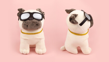 Two Plush soft beige pug dogs toys with sunglasses on pink background. Front view, side view, close-up.
