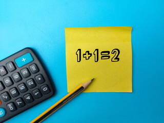 Calculator,pencil and sticky note with the number 1+1=2 on blue background.