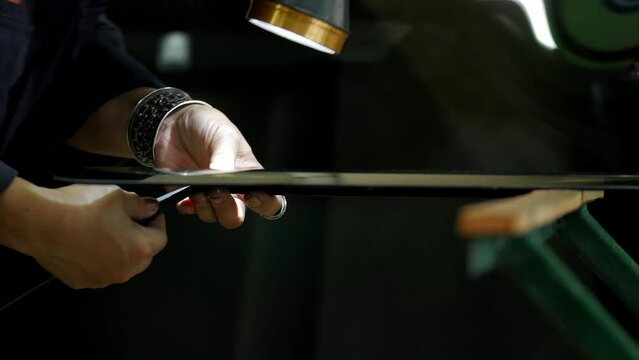 Process of preparing windshield for replacement in car service. A worker applies special adhesive sealant to the windscreen before installation on the auto.