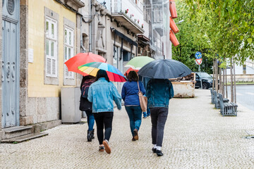 A group of people with umbrellas walk in the rain in a village in Portugal.