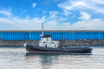Obraz premium The tugboat passes in the strait of the city port.