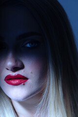 Fashion and make-up concept. Beautiful blonde woman portrait partly face covered with shadow. Mouth and nose illuminated with light. Model looking at camera. Red lipstick. Toned image with blue color