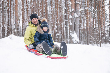 Father and little boy sledding and having fun in winter forest. Dad and son spending time together during walking in park.