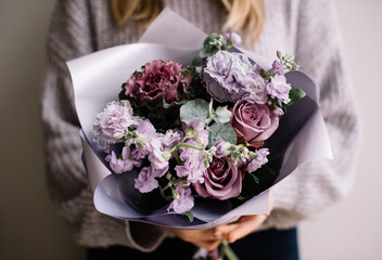 Very nice young woman holding  beautiful bouquet of fresh tender matthiola, brassica and rose flowers in purple colors, bouquet close up