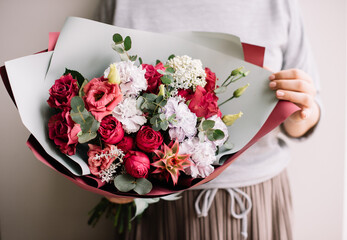 Very nice young woman holding big and beautiful bouquet of fresh roses, carnations, decorative pineapple, eustoma, eucalyptus flowers in red and pastel purple colors, cropped photo, bouquet close up