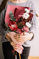Very nice young woman holding beautiful bouquet of fresh tender protea, carnations, cotton, eucalyptus flowers colors,  wrapped in red paper, bouquet close up - 555055595