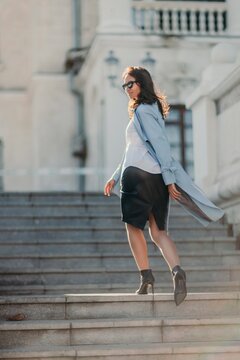 Woman walks in the city, lifestyle. Young beautiful woman in a loose light sweater, brown skirt and sneakers with a hat.