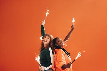 Pair of smiling, fun-loving friends celebrate and have a blast with sparklers and bengal lights in...