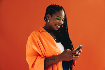 Vibrant, tech-savvy woman with dreadlocks smiles and uses her smartphone to browse the internet in a casual studio setting. - obrazy, fototapety, plakaty