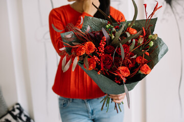 Very nice young woman in red sweater holding big and beautiful red bouquet of fresh roses, eustoma,
eucalyptus and other flowers, cropped photo, bouquet close up - 555058759