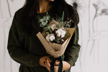 Very nice young woman holding beautiful bouquet of fresh cotton, eucalyptus, and other dry flowers in white and green colors, cropped photo, bouquet close up - 555058781