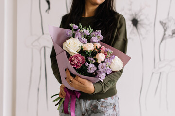 Very nice young woman holding big and beautiful bouquet of fresh roses, matthiola, carnations flowers in white and purple colors, cropped photo, bouquet close up